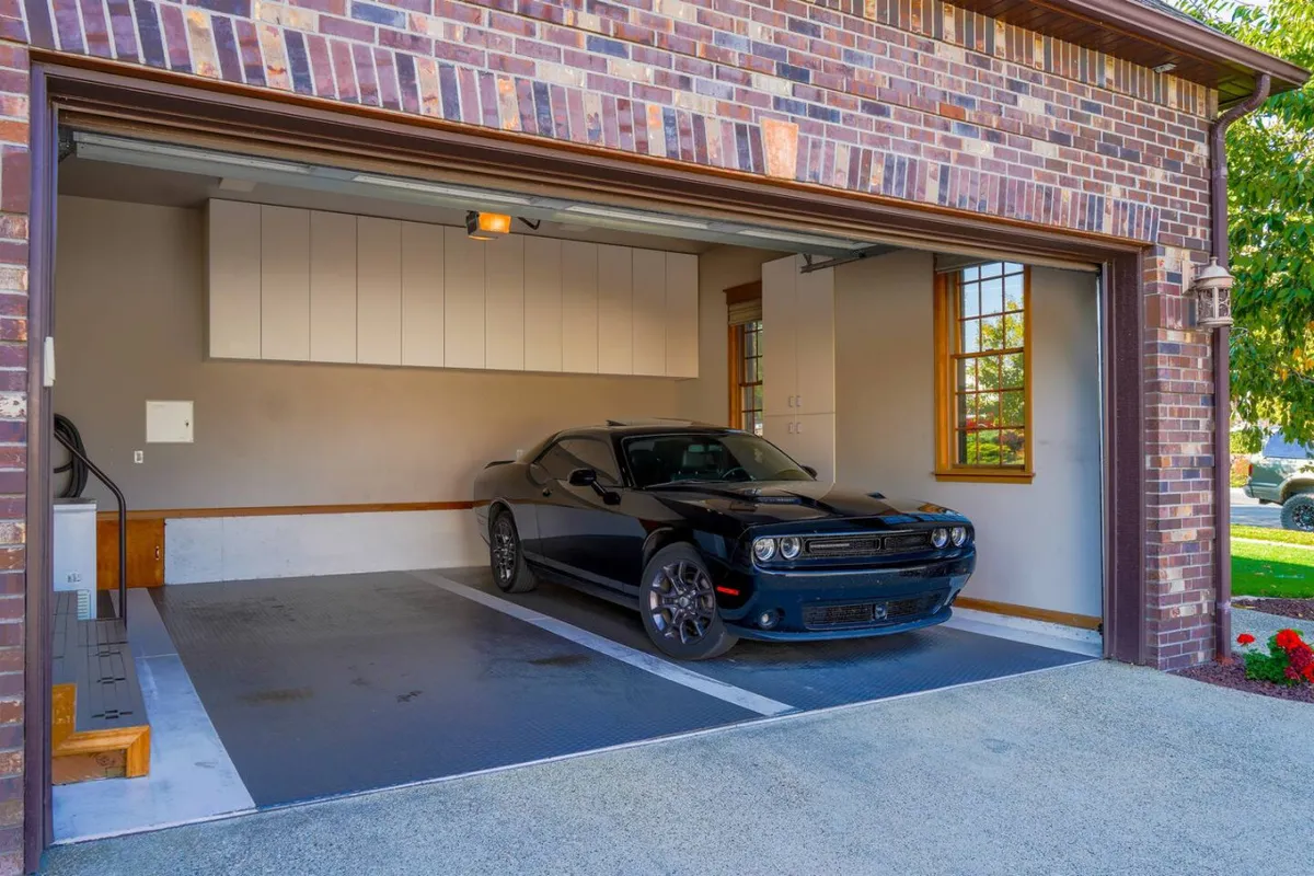 A pristine garage interior features a sleek black car, overhead storage cabinets, and a polished floor. The organized and modern space supports both secure parking and functional storage, reflecting the home's attention to convenience and security.