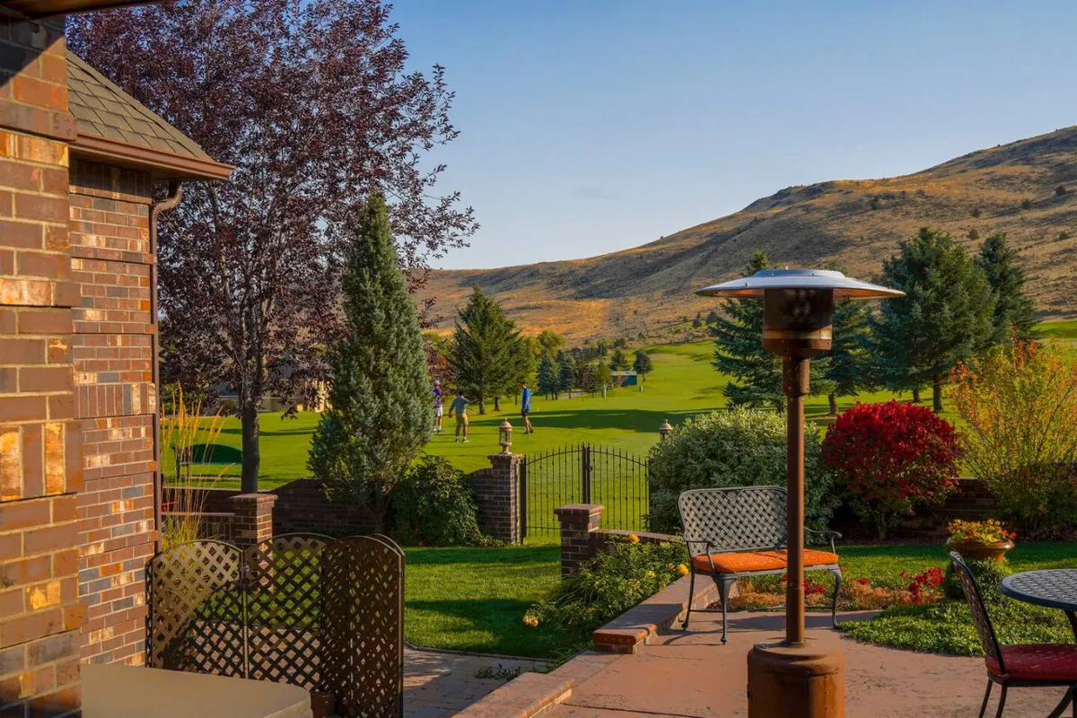 An expansive view over a beautifully landscaped backyard reveals an outdoor seating area with a direct line to the lush golf course and a stunning mountain backdrop. The scene captures the inviting transition from home to recreational spaces and illustrates access to exclusive outdoor amenities.