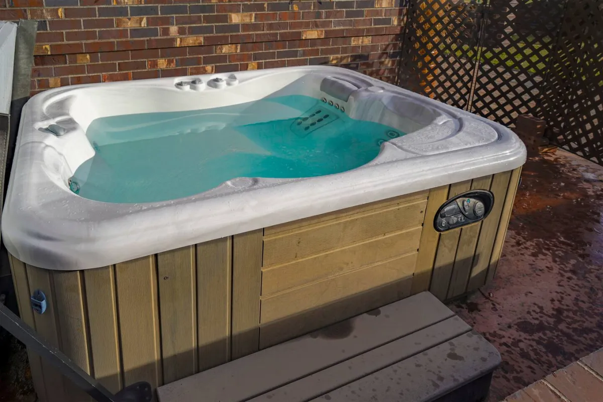 A serene hot tub set on a wooden deck against a backdrop of a brick wall, offering a calm and private retreat. The setting is peaceful and invites relaxation, particularly after a productive work session or during breaks between meetings.
