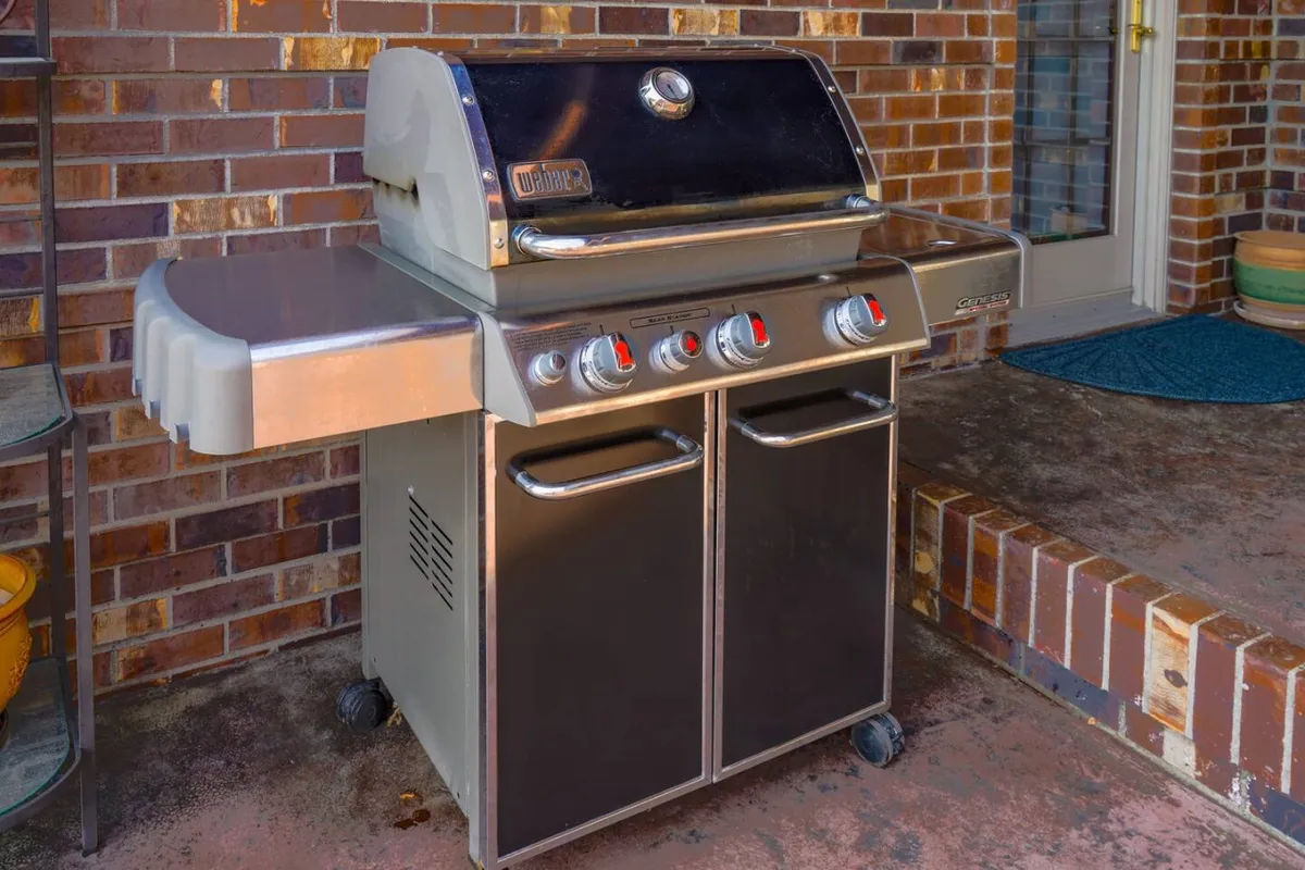 A BBQ grill is positioned against a brick wall, adjacent to a doorway, suggesting easy access from the home to the outdoor entertaining area. The scene is ideal for social gatherings and al fresco dining, reinforcing the pleasures of cooking and dining outdoors.