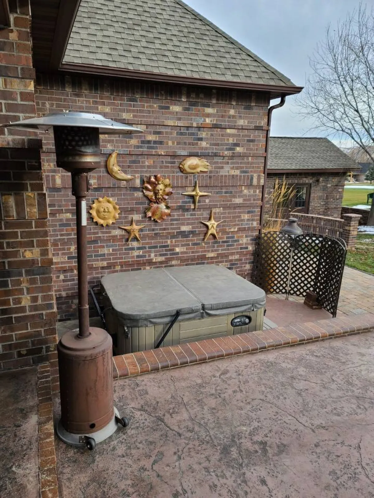 This image features a hot tub set against a decorative wall with outdoor heating and brickwork, creating a cozy and inviting spot for relaxation. The space is clearly designed for outdoor gatherings, with enough room for several guests to unwind while enjoying the fresh air.
