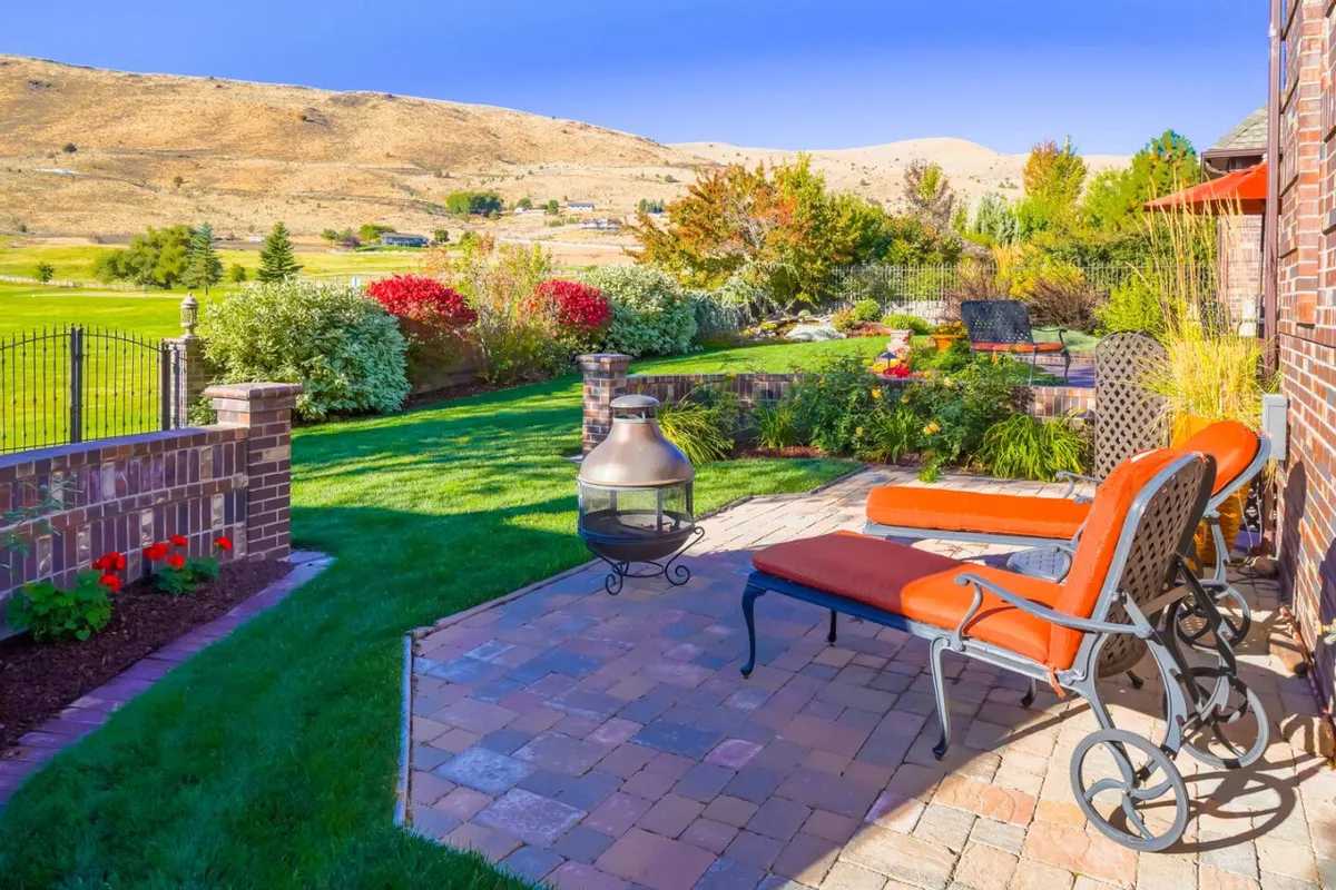The image showcases a tranquil outdoor lounge area with comfortable chairs, a fire pit, lush landscaping, and a scenic mountain view. The arrangement invites guests to relax or socialize, with nature providing a stunning backdrop.
