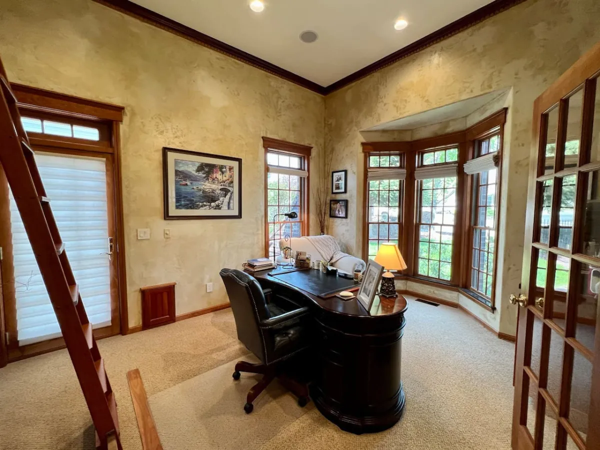 A tastefully appointed home office featuring a classic desk positioned by bay windows, accented with thoughtfully curated artwork. The workspace is bathed in natural light, creating an inspiring and focused environment ideal for productivity.