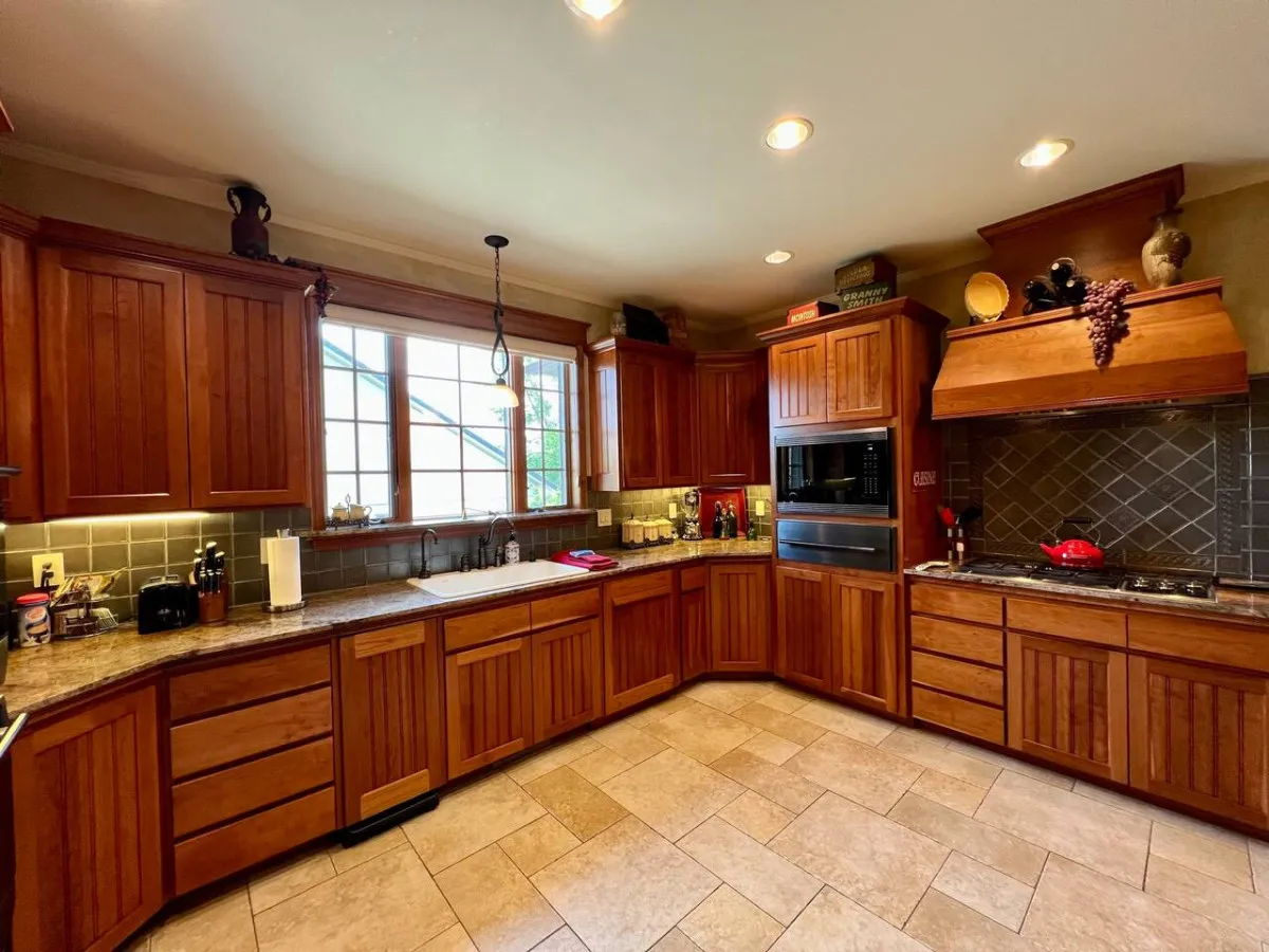 A warm, inviting chef’s kitchen featuring a prominent kitchen island, sleek wooden cabinetry, a large window with natural light, and gleaming stainless steel appliances. The setup hints at premium appliances and a layout perfect for both culinary artistry and social gatherings.