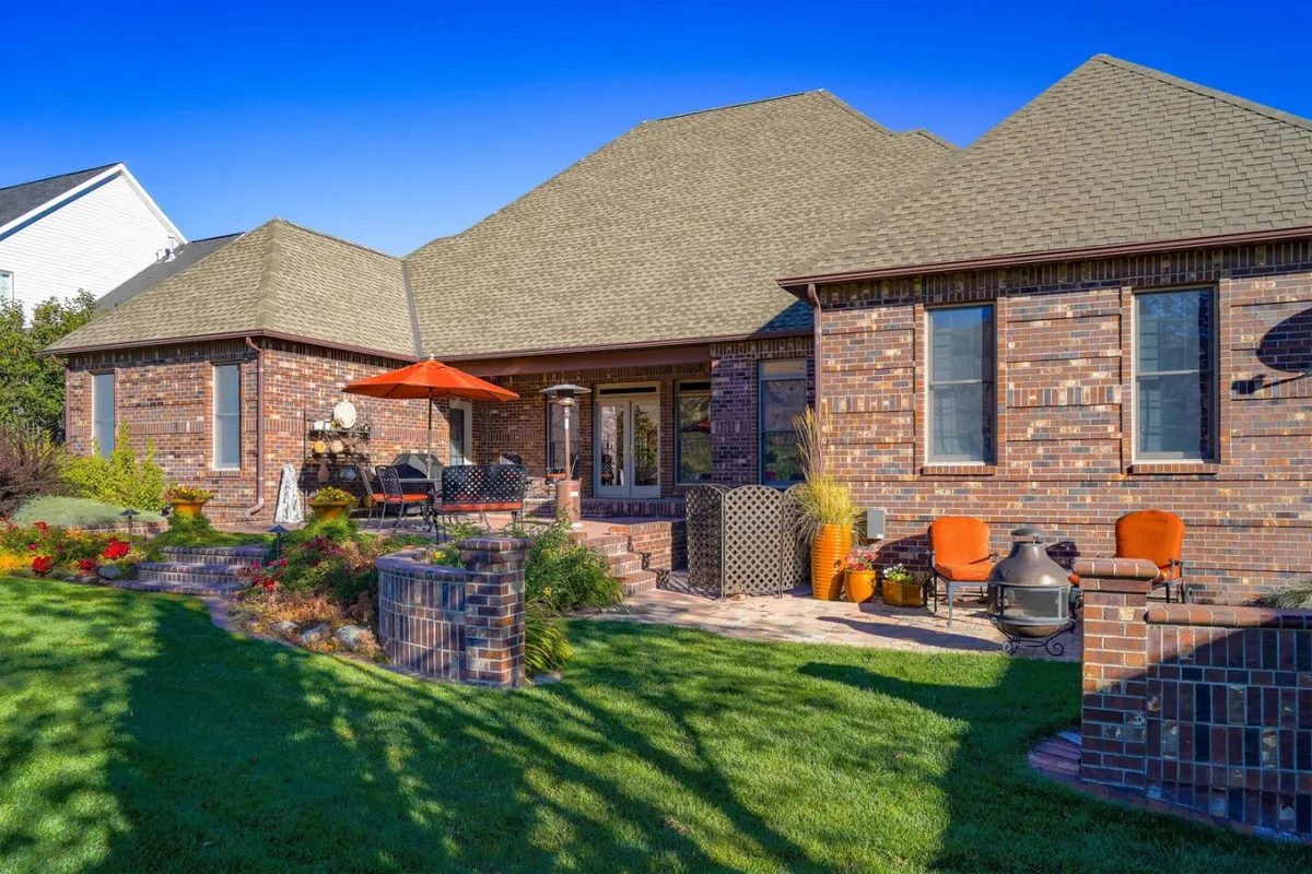 A welcoming outdoor patio and garden area with brick facade, decorative planters, and comfortable seating. The scene suggests a relaxed atmosphere perfect for al fresco dining or morning coffee.