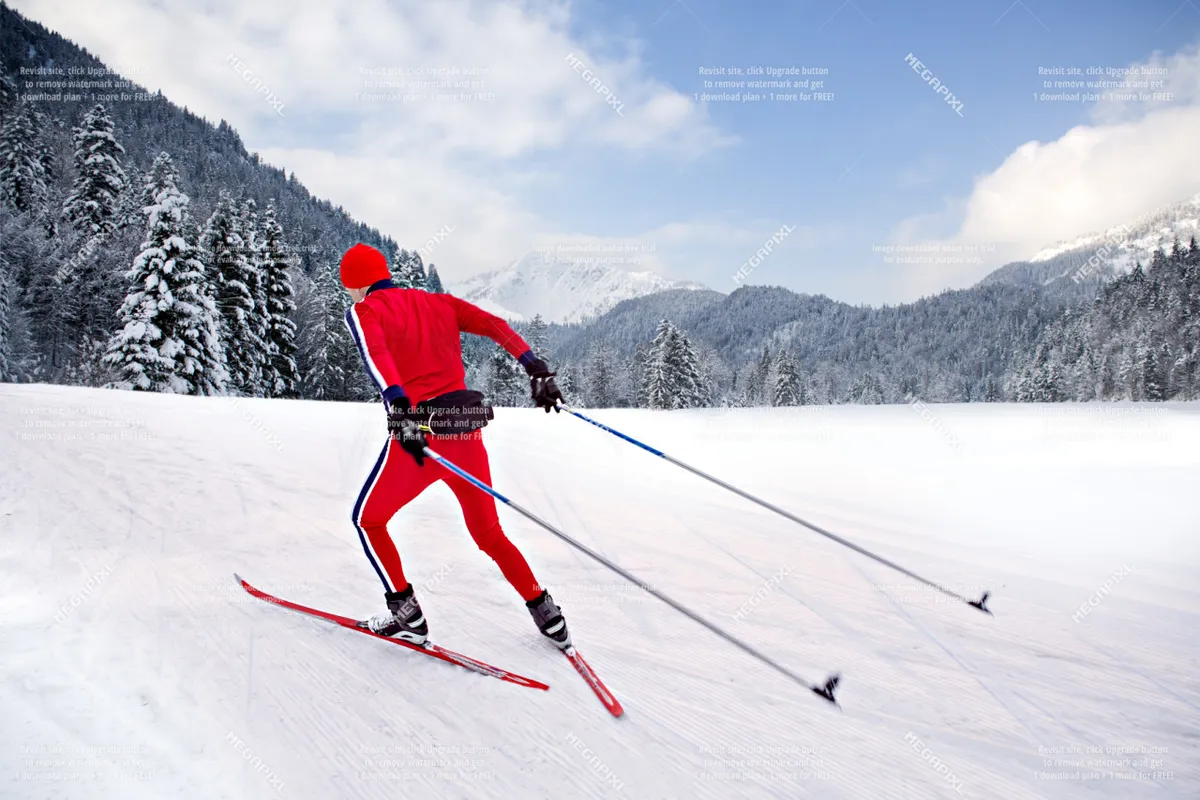 A cross-country skier glides through a pristine, snow-covered landscape with distant mountains rising under a bright sky. The expansive white terrain, dotted with trees, captures the exhilaration and beauty of winter sports in a natural setting.