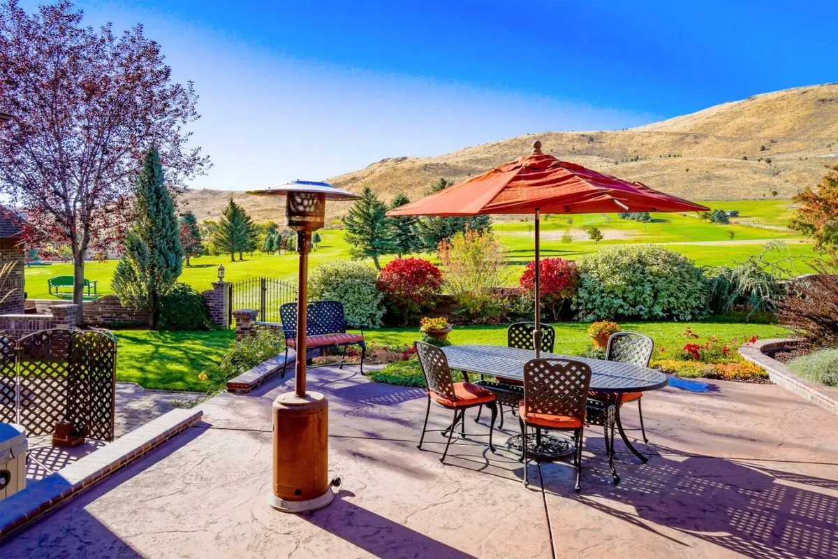 This scene displays an outdoor dining area with a red umbrella, surrounded by a landscaped garden and offering a broad mountain view. The cheerful setup is ideal for barbecues, sunset dinners, or enjoying morning coffee outdoors.